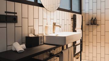 A modern bathroom with a large mirror, white tiled walls, a wooden floor, and a black vanity with a sink and towel rack.