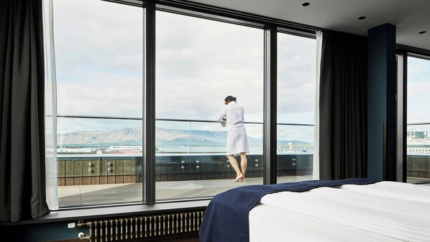 A hotel room with a large window, a bed, and a view of a cityscape. - Exeter Hotel (Reykjavik)