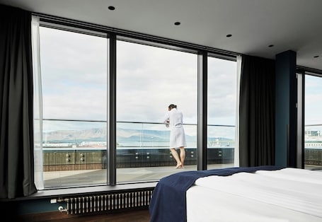 A hotel room with a large window, a bed, and a view of a cityscape.