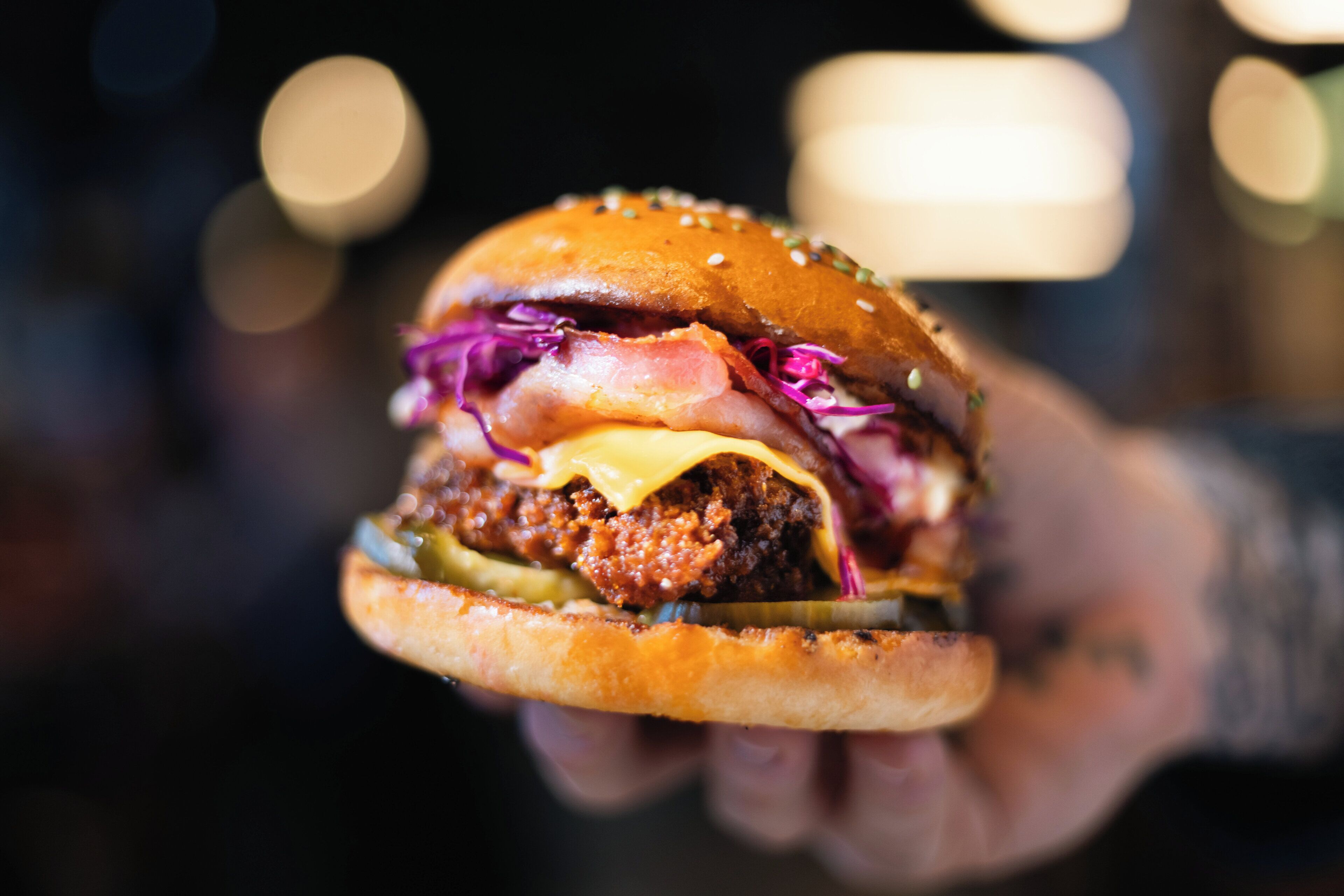 Ein Detailfoto eines Burgers, bei dem die Zutaten wie ein Rinderpatty, Käse, Speck und Gurken deutlich erkennbar sind.