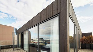 A modern building with large glass windows, a wooden deck, and a view of a ship. - Exeter Hotel (Reykjavik)