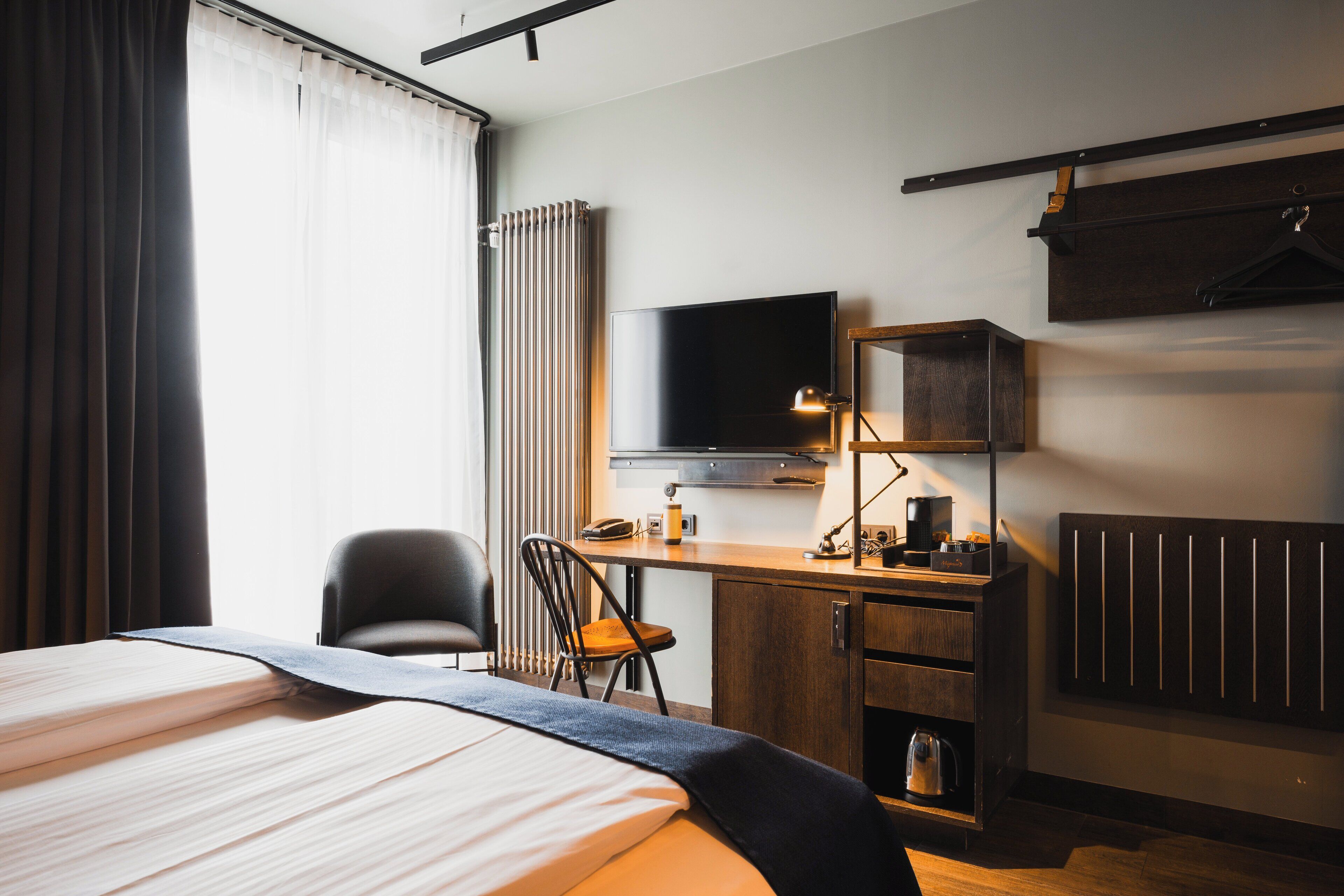 Una habitación de hotel con cama, escritorio con computadora, silla, televisor y radiador.