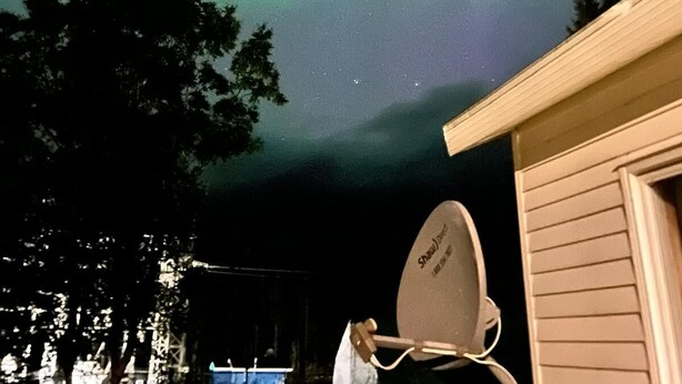 A satellite dish attached to a house with a view of the night sky.
