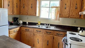 A kitchen with wooden cabinets, a stainless steel sink, a stove, and a window with curtains.