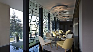 A modern interior with a glass partition, round tables, and chairs. - Hotel ZENA beauty & shopping center (Hévíz)