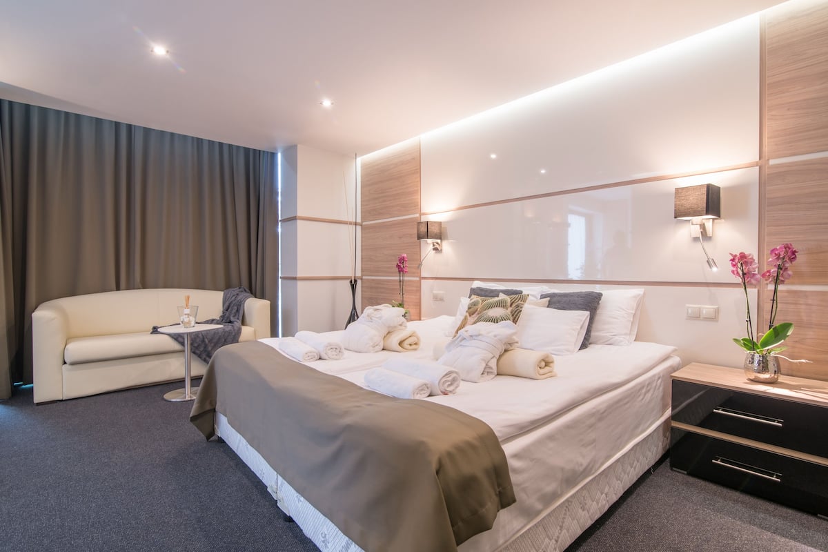 Ein modernes Hotelzimmer mit einem großen Bett, einer Couch, einem kleinen Tisch und einem Nachttisch mit Blumen in einer Vase.