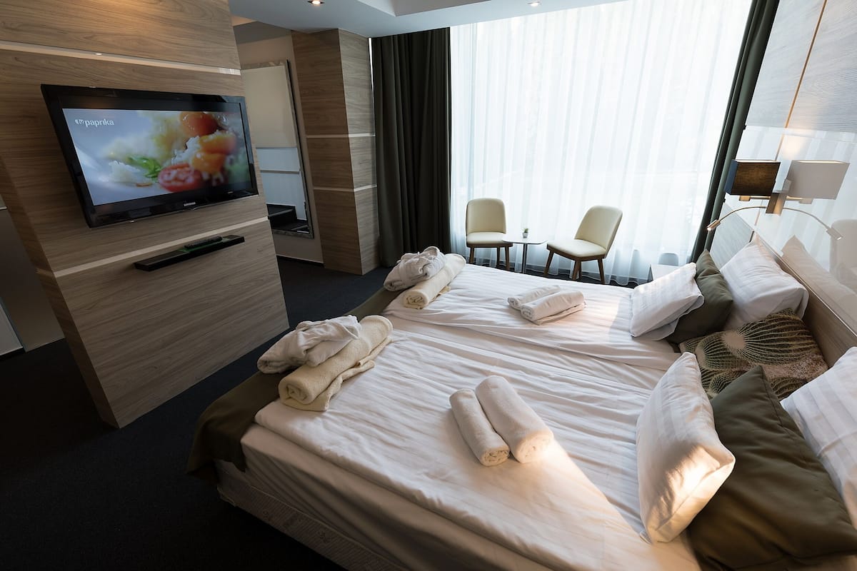 Ein Hotelzimmer mit Bett, zwei Stühlen, einem Fernseher und einem Fenster mit Vorhängen.