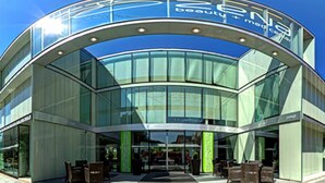 A modern building with a curved glass facade and a sign that reads "EENA beauty + med center". - Hotel ZENA beauty & shopping center (Hévíz)
