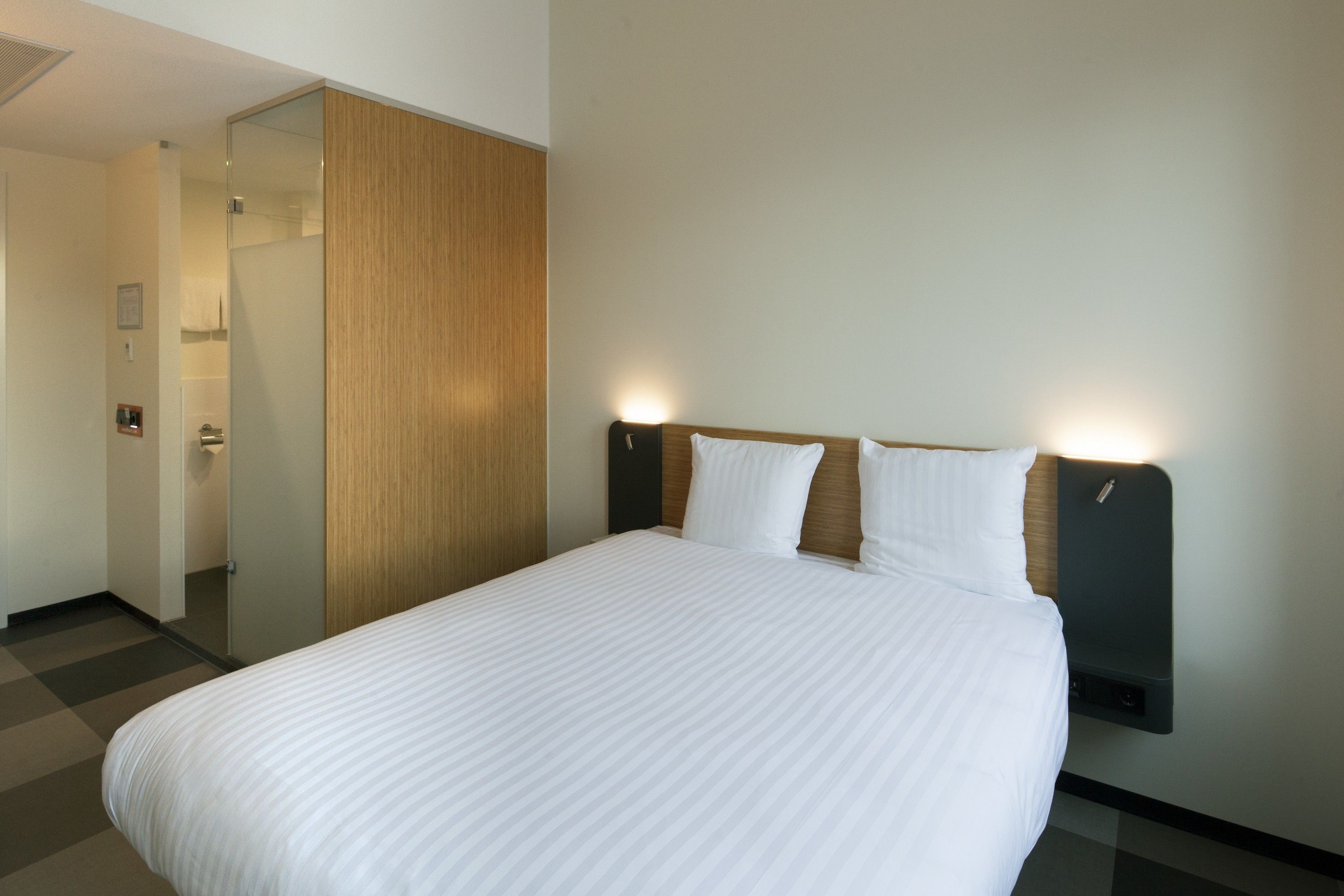 Habitación de hotel con una cama grande, un armario de madera y una mesita de noche fijada a la pared.