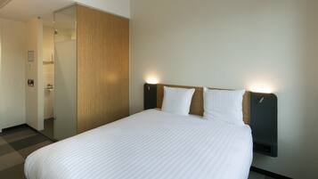 Habitación de hotel con una cama grande, un armario de madera y una mesita de noche fijada a la pared.
