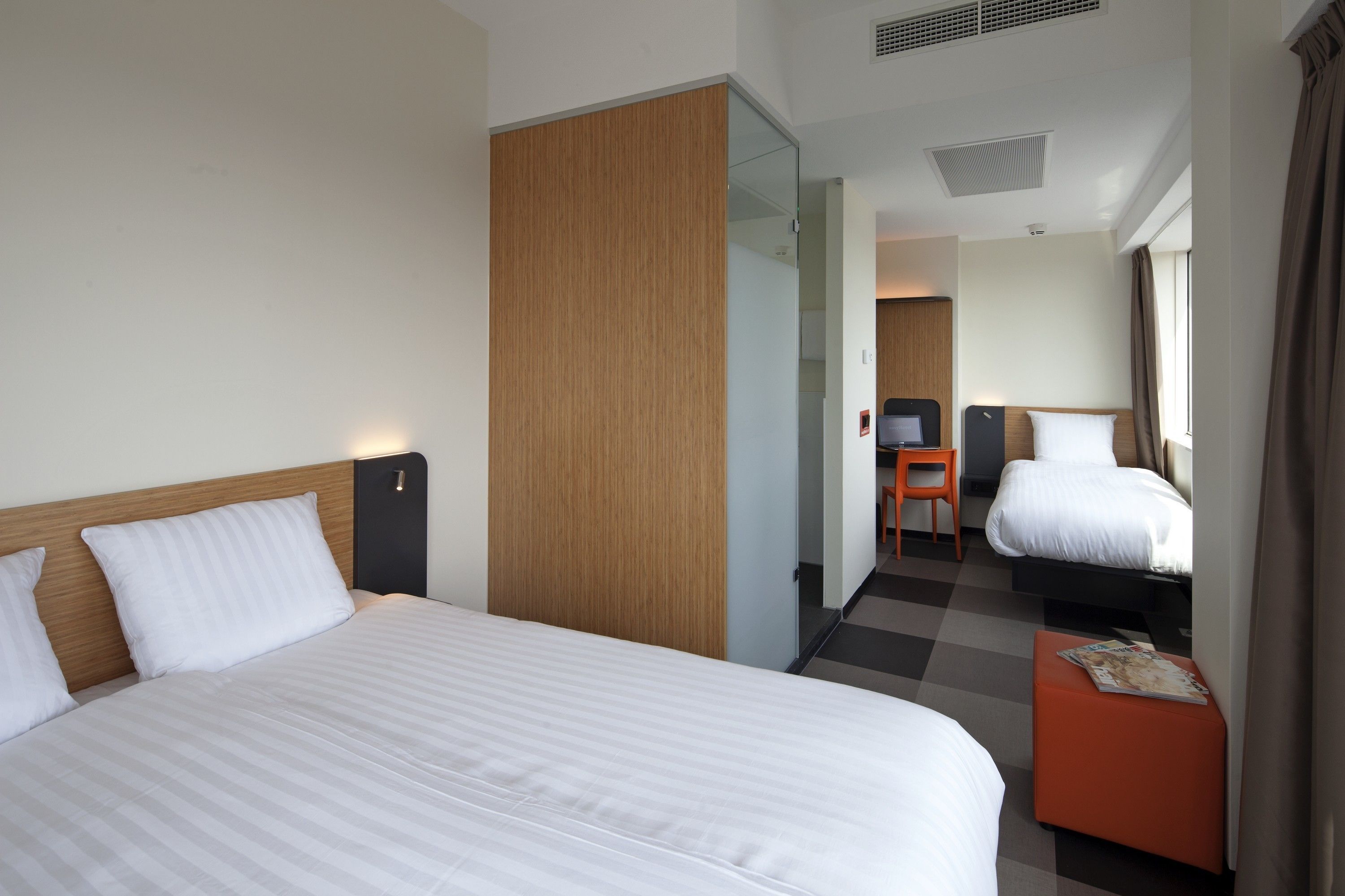 Een hotelkamer met twee bedden, een houten kledingkast, een klein tafeltje met een tijdschrift en een bureau met een stoel.