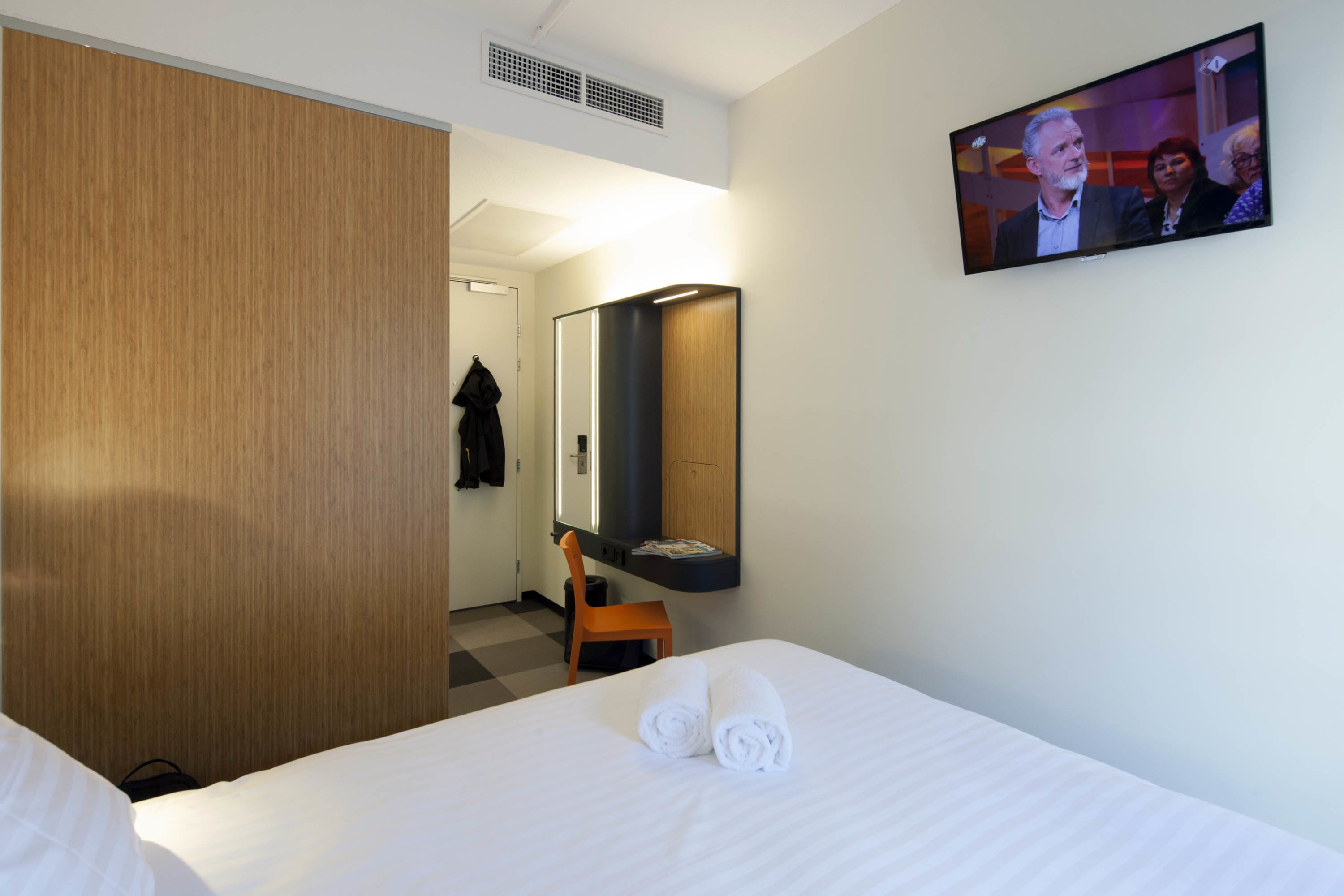 Une chambre d’hôtel avec un lit, une télévision, un miroir et une armoire en bois.