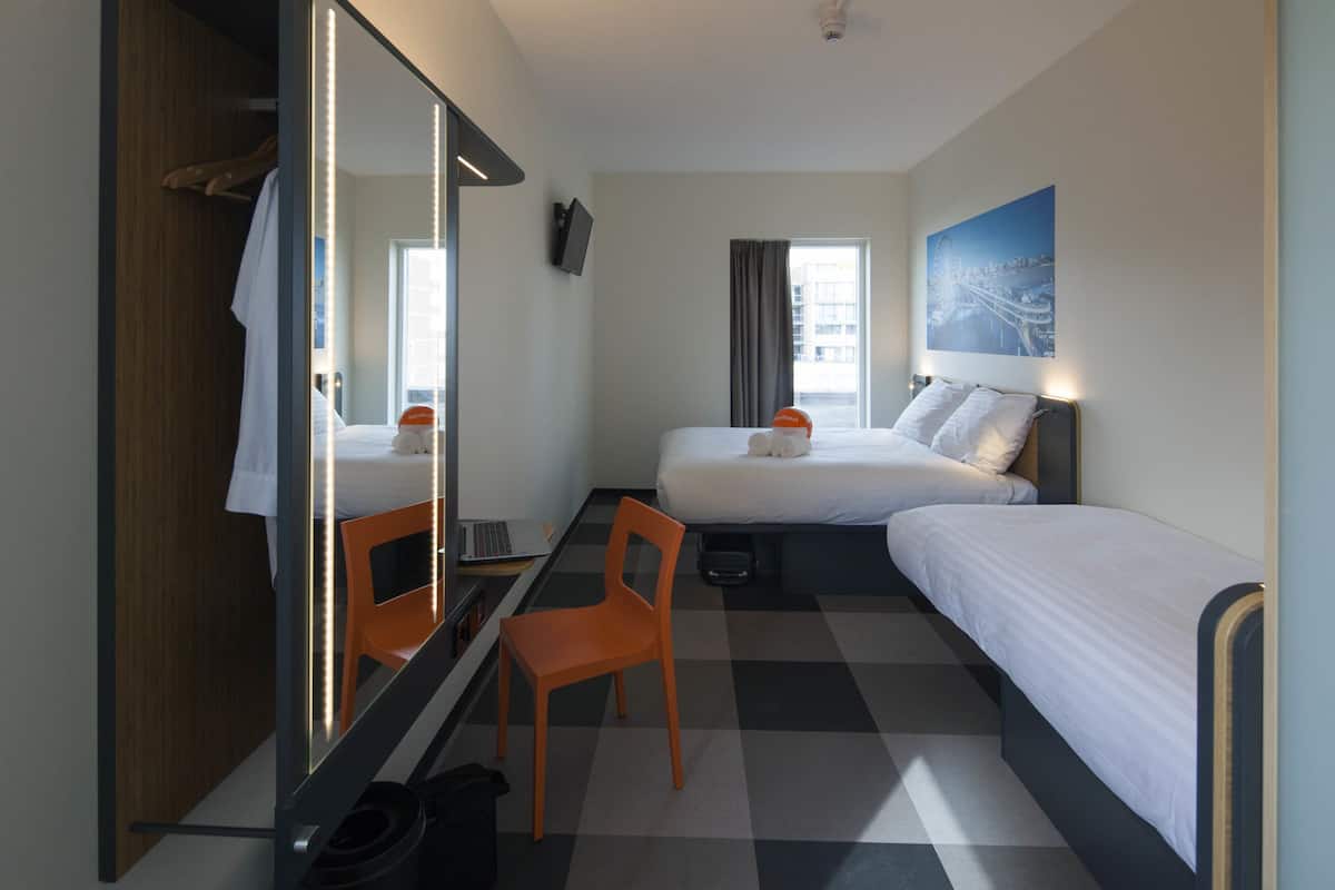 Een hotelkamer met twee bedden, een bureau, een stoel, een spiegel en een raam met gordijnen.