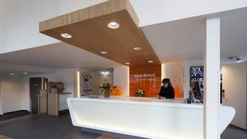 Ein moderner Hotel-Empfangsbereich mit Holzbalkendecke, einem weißen Empfangstresen und einem Schild mit der Aufschrift 'easyHotel Scheveningen'.