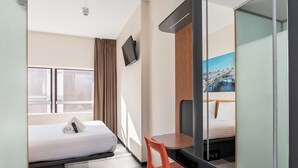 Een hotelkamer met een bed, een bureau, een stoel, een televisie en een grote spiegel die een stadszicht weerspiegelt.