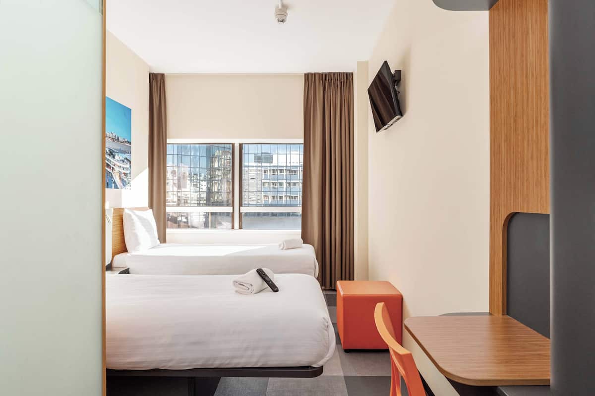 Hotelkamer met twee bedden, een bureau, een stoel, een televisie en een raam met uitzicht op de stad.
