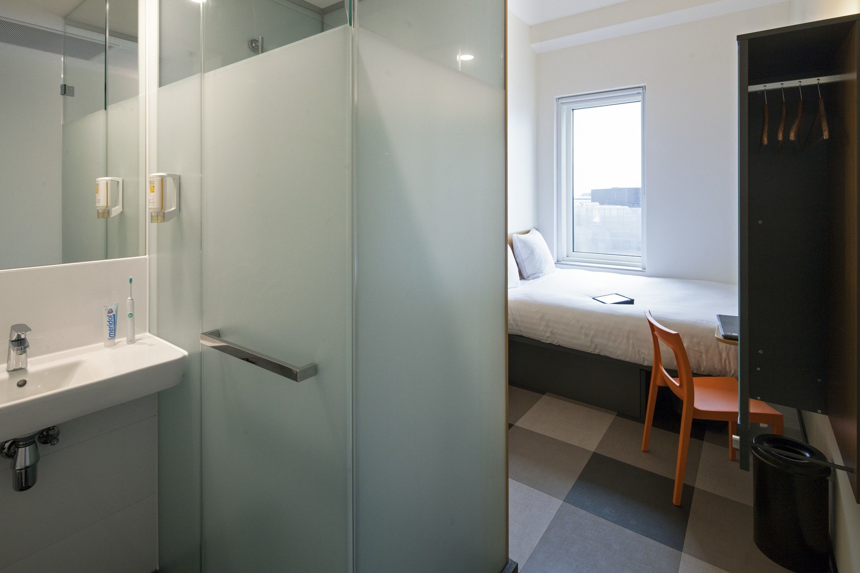 Et moderne badeværelse med bruseafskærmning i glas, vask med toiletartikler og seng med udsigt fra vinduet.
