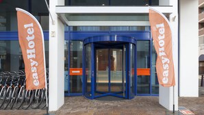 Een hotelingang met een draaideur en twee oranje banners.