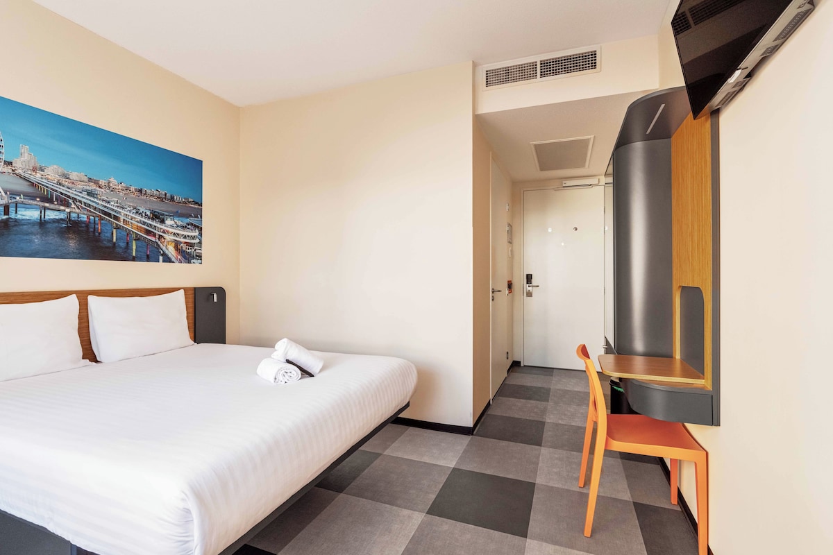 Une chambre d’hôtel avec un lit, une télévision, un bureau et un tableau représentant un pont.