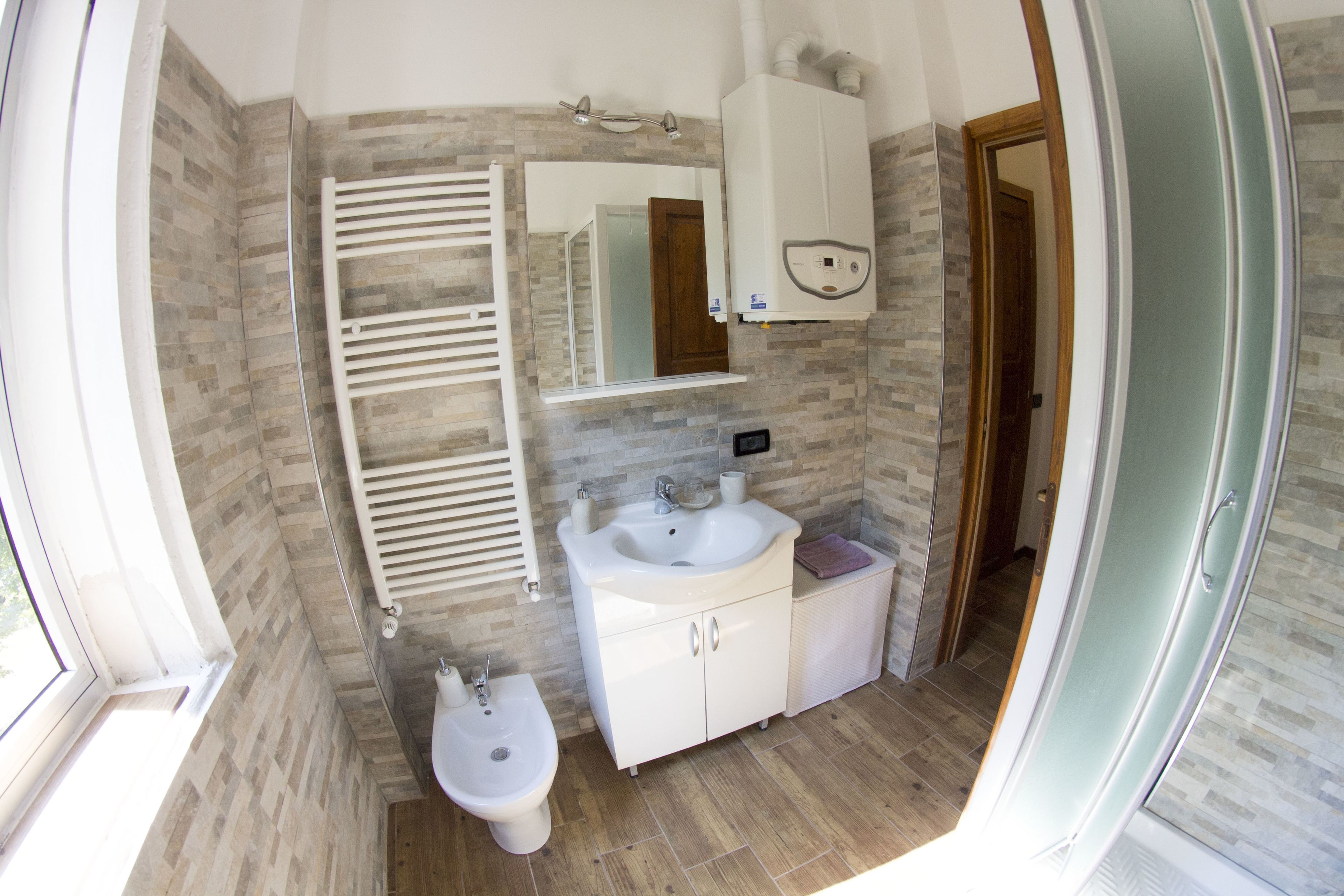 Een badkamer met een witte wastafel, een hygiëneschuimer, een handdoekhouder, een spiegel en een douchedeur.