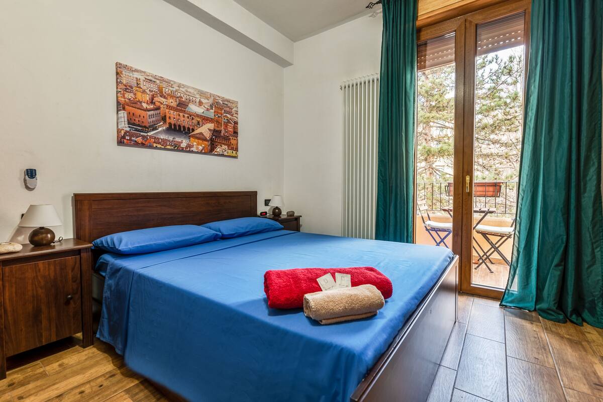 A bedroom with a bed, a nightstand, a lamp, a painting, and a sliding glass door to an outdoor area.