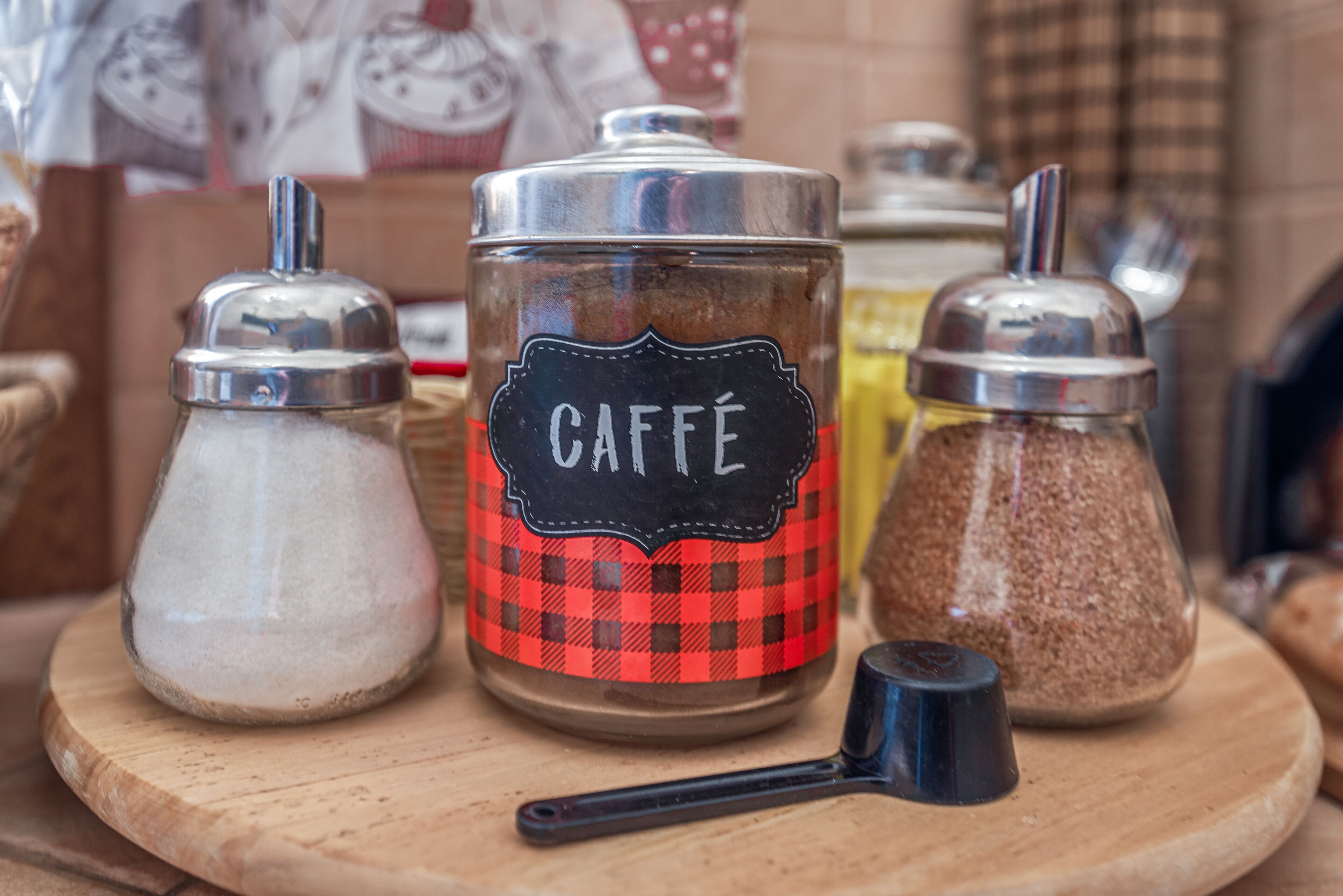 Tres recipientes sobre una tabla de madera, uno etiquetado como "CAFFÉ" con un estampado a cuadros rojo y negro.