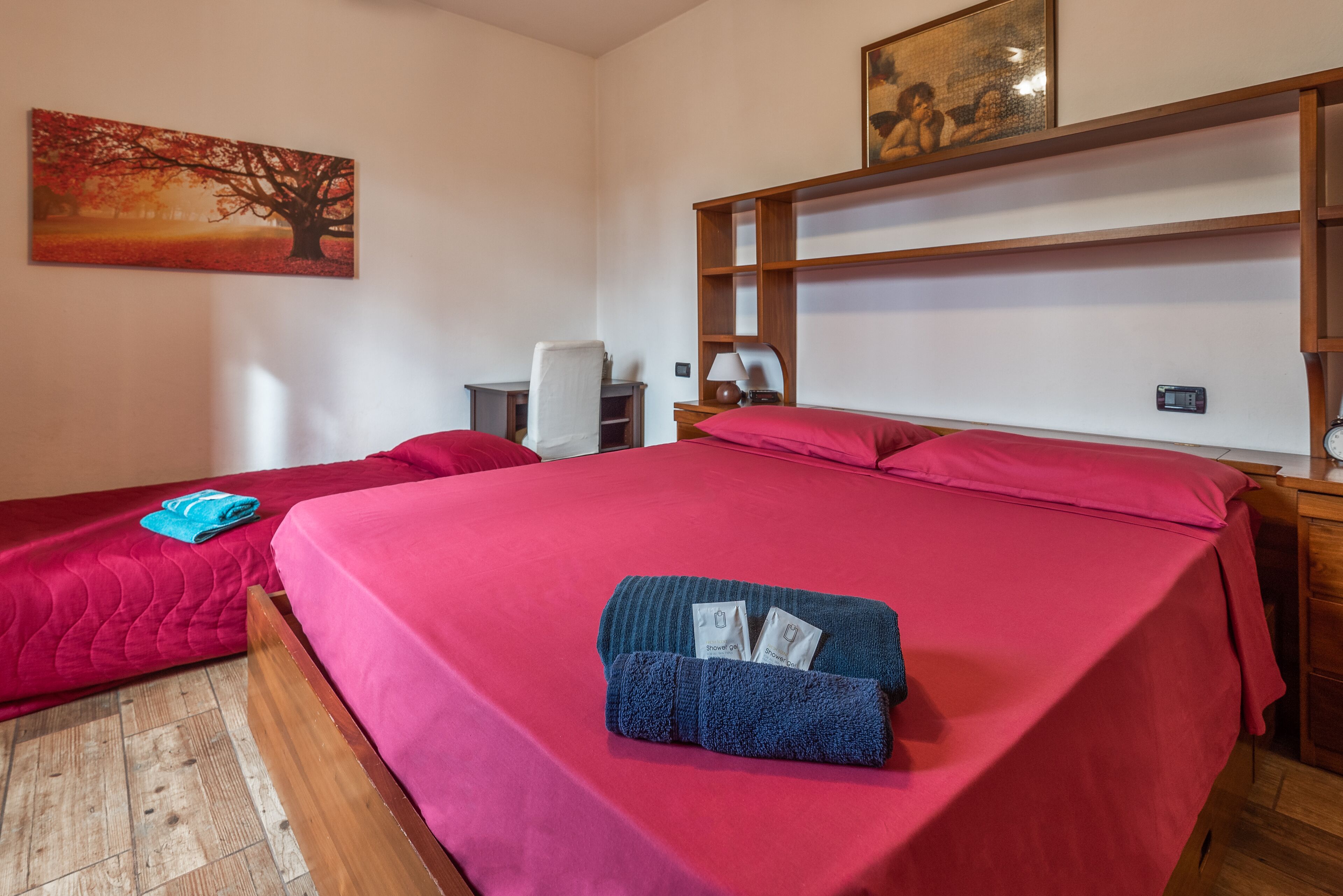 Habitación de hotel con dos camas, un escritorio, una silla y una estantería con un cuadro.