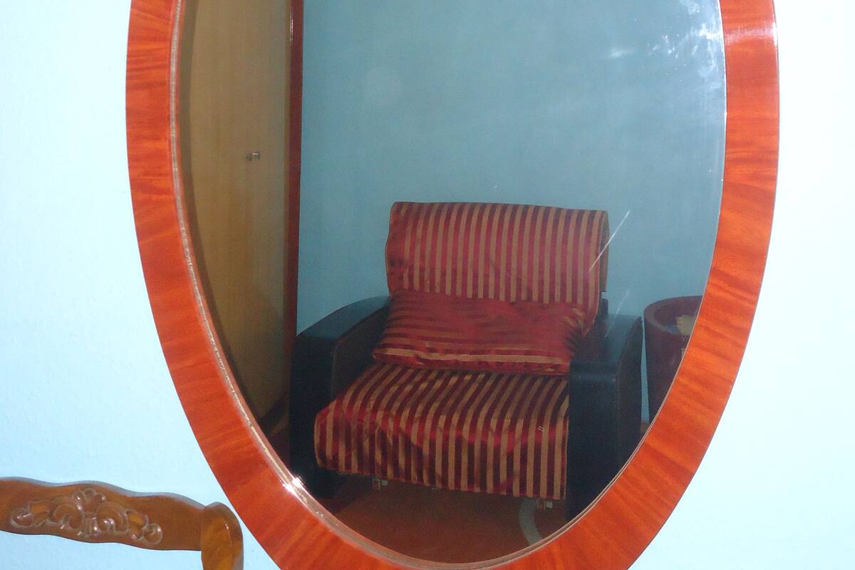 A room with a large oval mirror on the wall, a wooden chair, and a striped sofa.