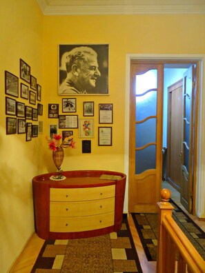 A hallway with a wooden door, a wall decorated with framed pictures and certificates, and a wooden console table with drawers. - Albatros (Tbilisi)