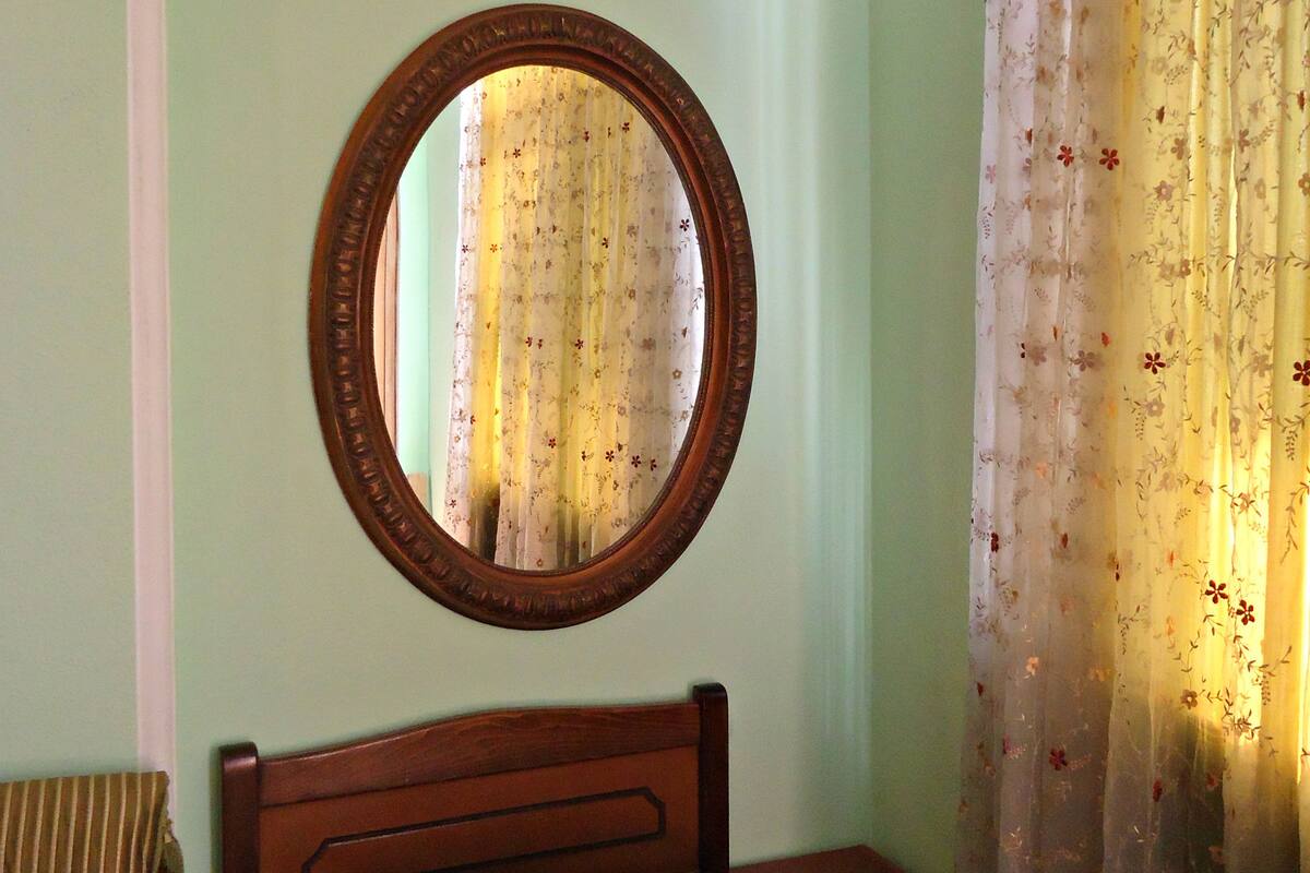 A bedroom with a wooden headboard, a bed with a plaid bedspread, a nightstand, a chair, and a mirror on the wall.