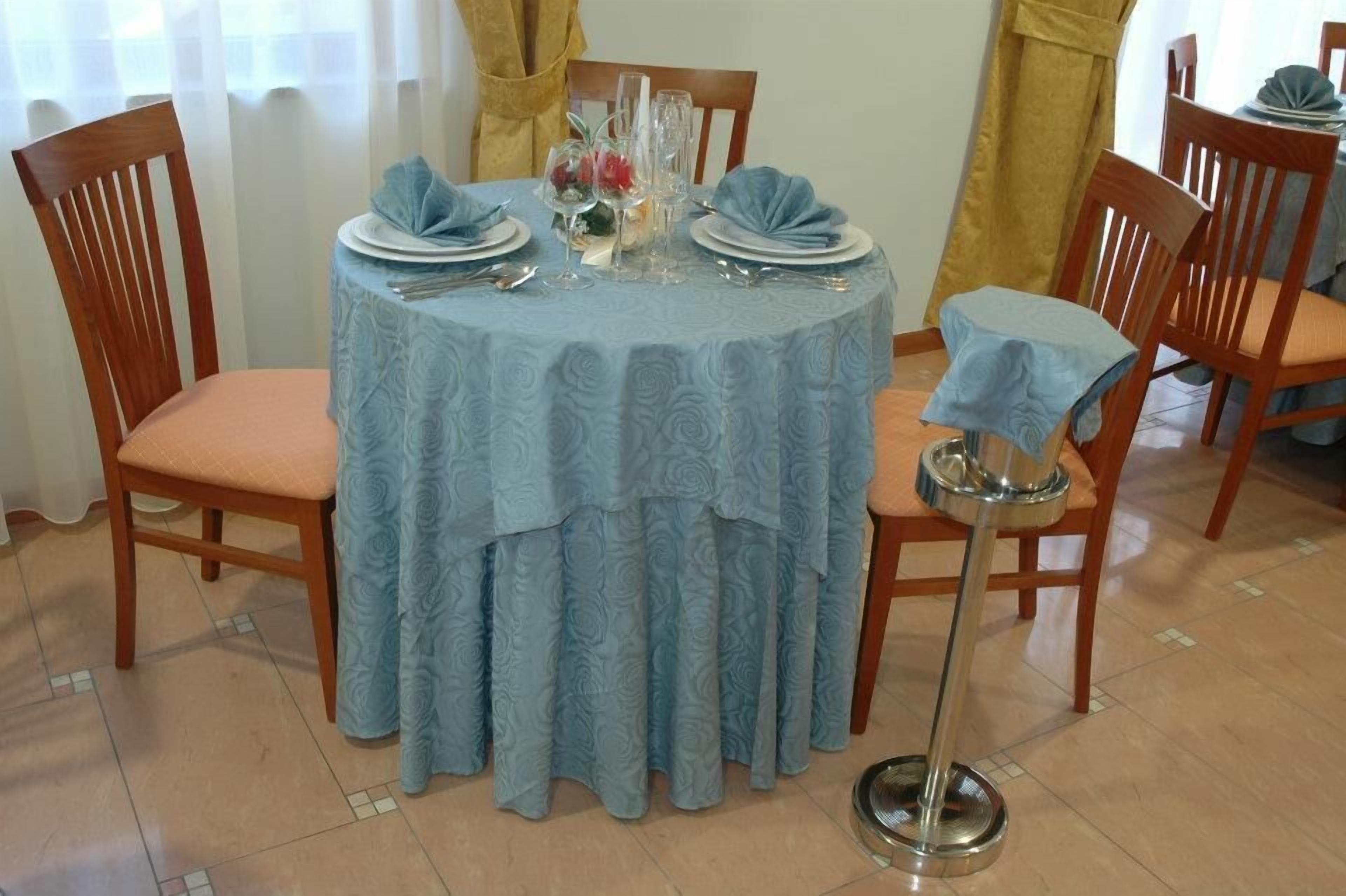 A round dining table with a blue tablecloth, surrounded by wooden chairs with cushions.