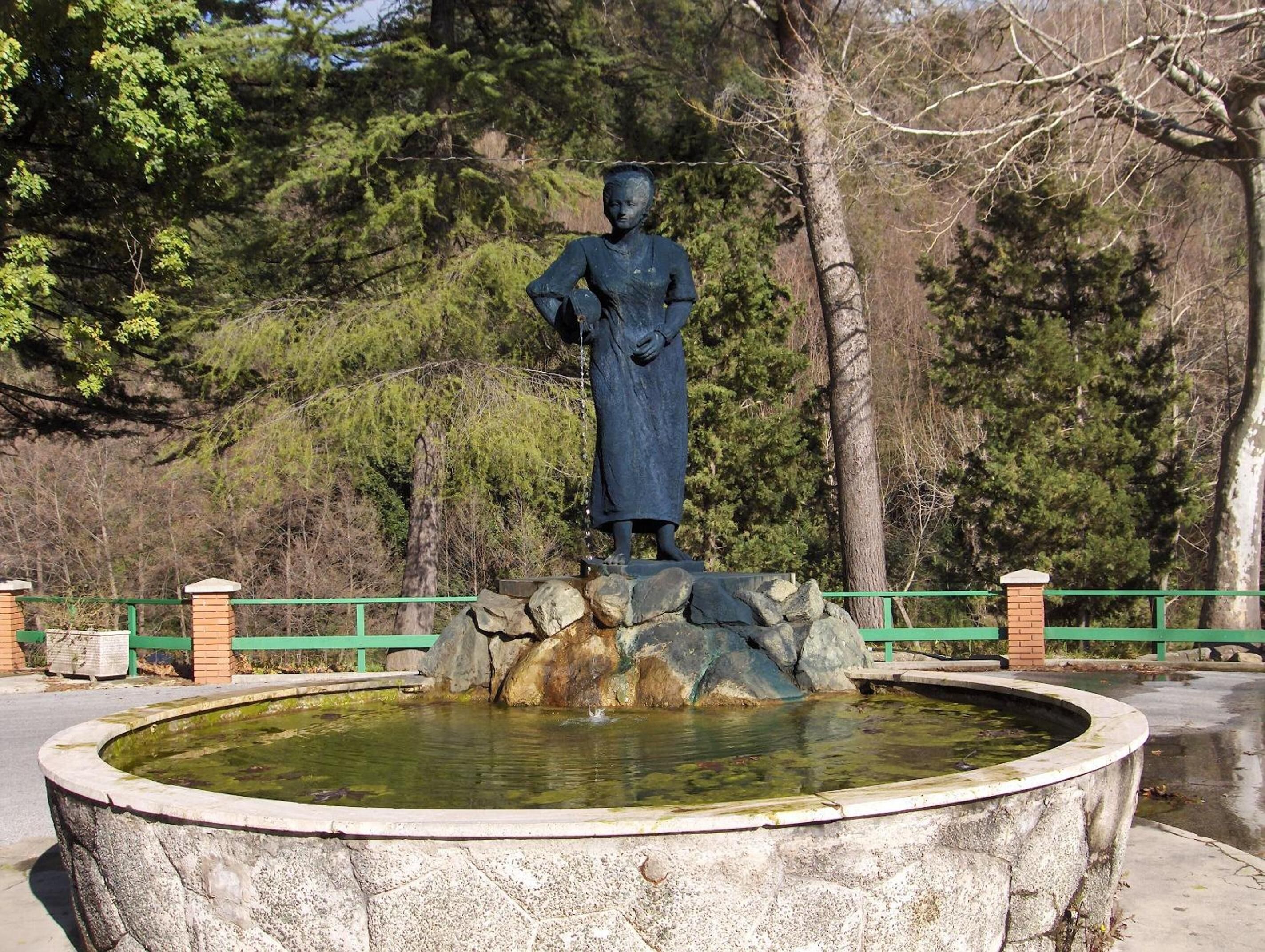 A statue of a woman on a pedestal with a circular stone fountain in front.