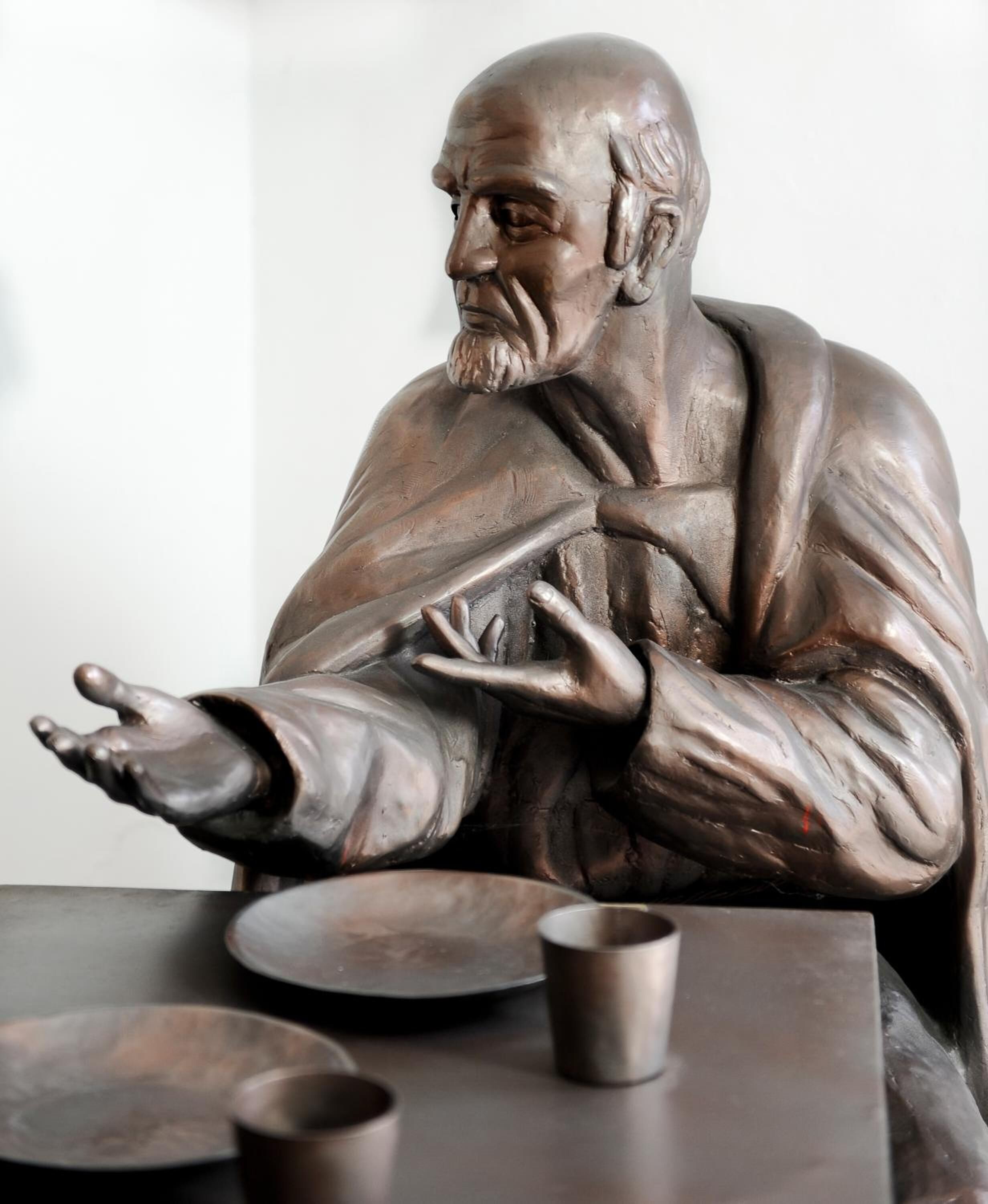 Une statue en bronze représentant une figure assise, les bras tendus, placée sur une table avec une tasse et un bol.