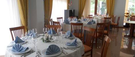 Un comedor con mesas redondas dispuestas para una comida, con manteles blancos y servilletas azules.