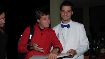 A man in a red jacket holding a tablet, standing next to a man in a white suit with a blue bow tie.