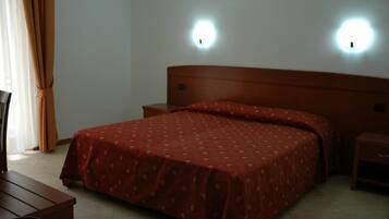 A hotel room with a bed, nightstands, a wooden desk, and two wall-mounted lights.