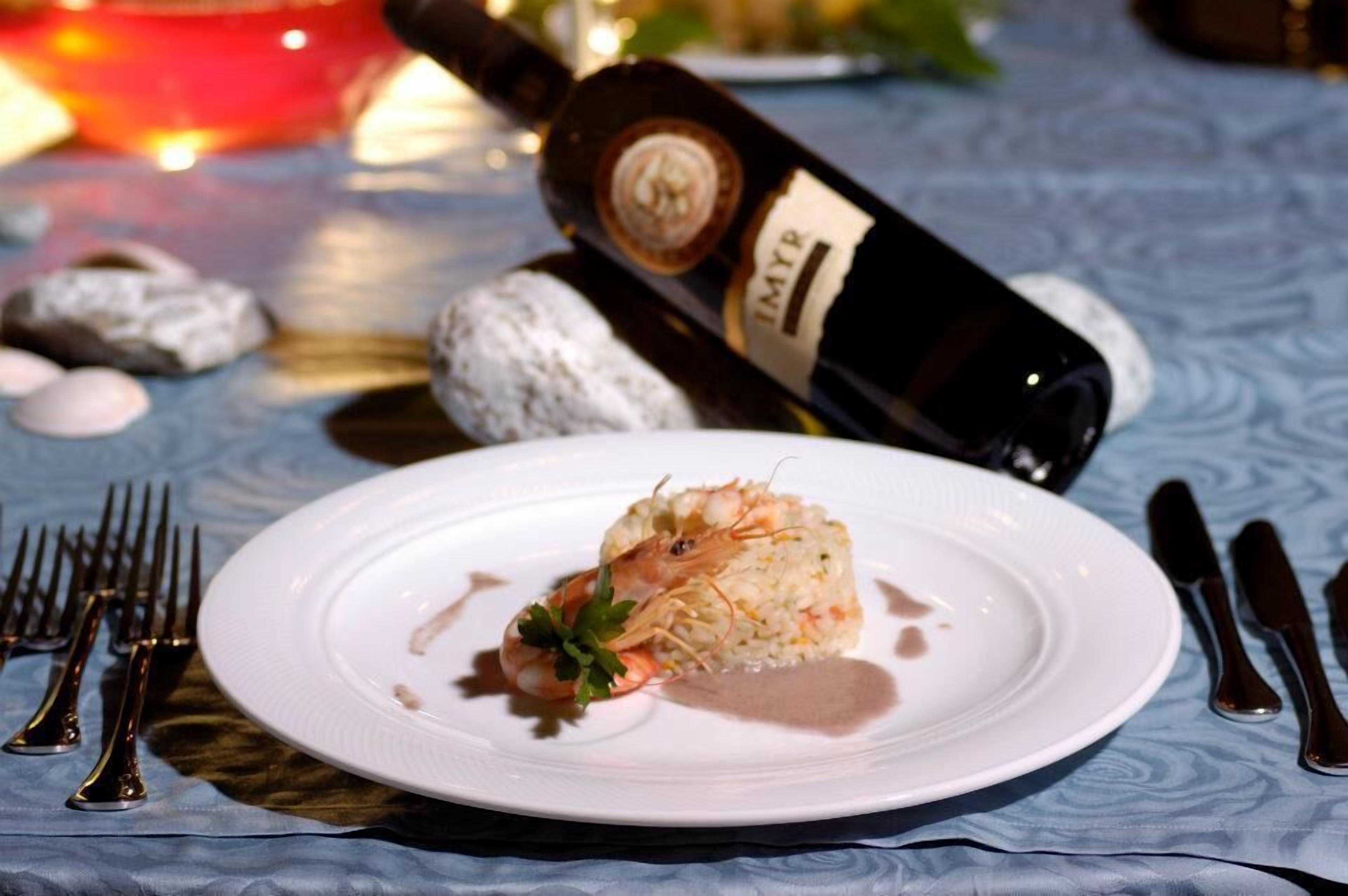 Un plato de camarones con arroz y una botella de vino al fondo.