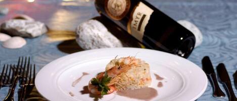 Un plato de camarones con arroz y una botella de vino al fondo.