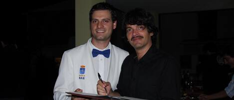 Dos hombres, uno con bata blanca y placa, sosteniendo una tableta y un bolígrafo.