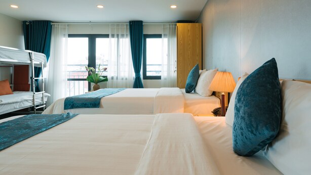 A hotel room with two beds, a bunk bed, a potted plant, and a window with curtains. - Hanoi Prime Center Hotel (Hanoi)