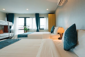 A hotel room with two beds, a bunk bed, a potted plant, and a window with curtains.