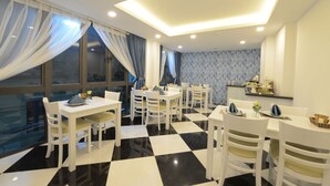 A dining area with white tables and chairs, a checkered floor, and a view of the city through large windows. - Hanoi Prime Center Hotel (Hanoi)