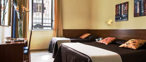 A hotel room with two beds, a desk, a chair, a window with curtains, and artwork on the wall.