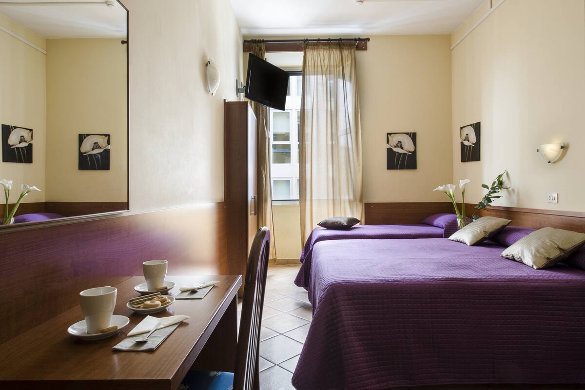 A hotel room with two beds, a TV, and a dining area with a table and chairs.