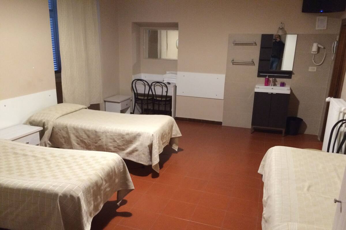Una habitación con tres camas, un escritorio, una silla, un espejo, un lavabo y un radiador.