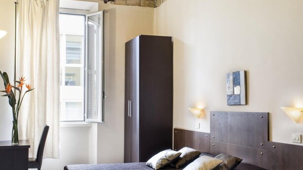 A bedroom with a brick ceiling, a bed with pillows, a wardrobe, a desk with a chair, and a window with curtains. - Cervia - The Hostel (Rome)