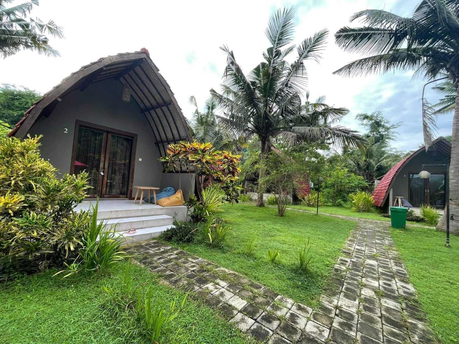 Uma casa de dois andares com um telhado curvo, cercada por vegetação exuberante e palmeiras.