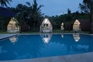 A pool area with a clear blue water surface, surrounded by palm trees and a few small, dome-shaped structures with open doors. - Apit Lawang Villas (Penida Island)