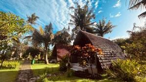 A small, single-story building with a tiled roof, surrounded by lush greenery and palm trees. - Apit Lawang Villas (Penida Island)