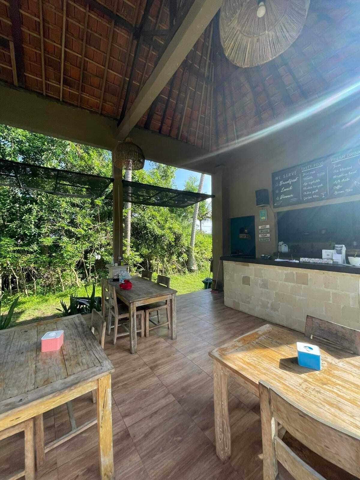 An outdoor dining area with wooden tables and chairs, a menu board, and a view of lush greenery.